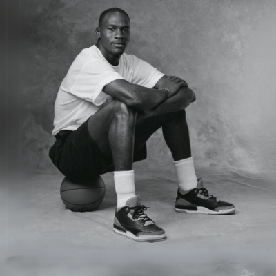 A man sitting on a basketball ball posing with Air Jordan 3 sneakers