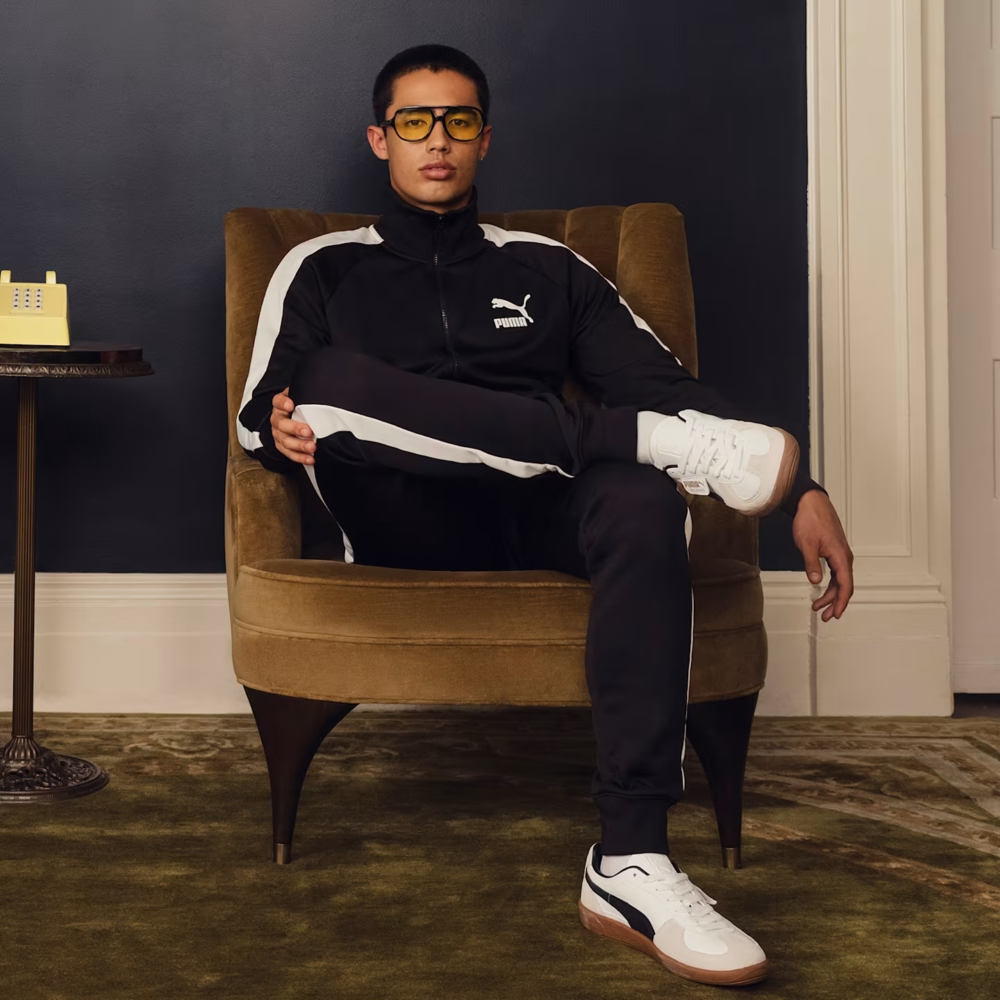 Puma Male Model wearing a Puma tracksuit and sitting on a chair