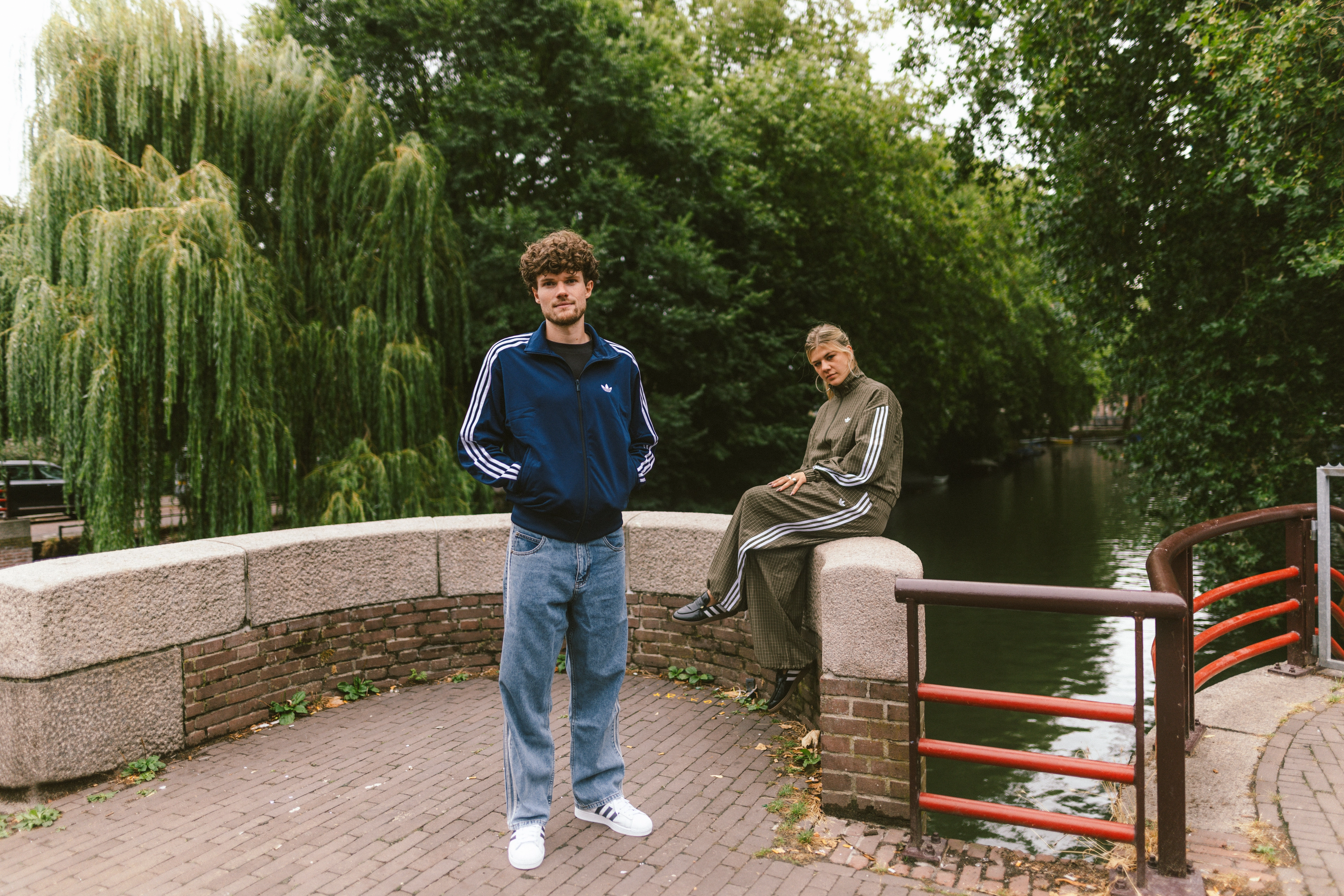 Twee modellen die poseren op een brug in adidas kleding en schoeisel.